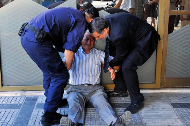 An crying elderly man is assisted by an employee and a policeman outside a national bank branch as pensioners queue to get their pensions, with a limit of 120 euros, in Thessaloniki on 3 July, 2015. (Photo by Sakis Mitrolidis/AFP Photo)