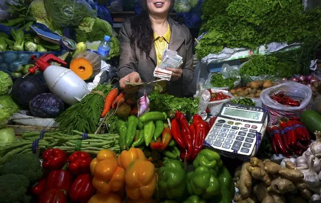 A fruit and vegetable stall owner uses a calculator to work out prices for a customer at a small market in central Beijing, China July 7, 2011. (Photo by David Gray/Reuters)