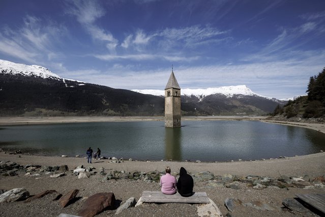 The church spire of the submerged village of Graun protrudes from the Reschensee lake, which has been nearly completely drained, during construction work of a new alpine road on April 29, 2024 near Resia, Italy. The six kilometer long lake, located in the German-speaking region of South Tyrol, is a reservoir formed from the construction of a nearby dam in the 1950s and submerged the village of Graun. A road runs along its edge, though increasing instability of mountain rock above is making its continued use too dangerous. The new road will run approximately 50 meters away and into the lake, which is requiring construction crews to move massive amounts of sand from the lake's floor to create a berm for the new road. A warming climate is melting permafrost that binds rock inside mountains across the European Alps, threatening many alpine passages. Once the new road is completed authorities will restore Reschensee with water. (Photo by Jan Hetfleisch/Getty Images)