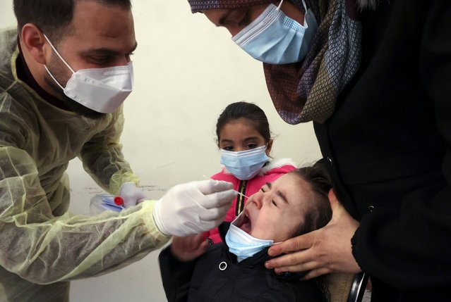 A medic from the Palestinian Health Ministry takes a swab sample from a child to test for the coronavirus, in the village of Dura west of Hebron, in the Israeli-occupied West Bank, on January 23, 2022. (Photo by Hazem Bader/AFP Photo)