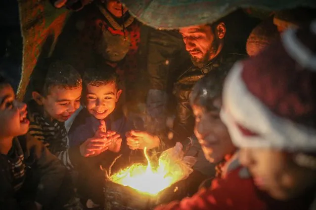 Refugee Syrian kids gather around fire to stay warm in a camp during winter season in Idlib, Syria on January 26, 2022. Civilians are forced to burn their clothes to stay warm at night, due to harsh winter conditions. (Photo by Muhammed Said/Anadolu Agency via Getty Images)