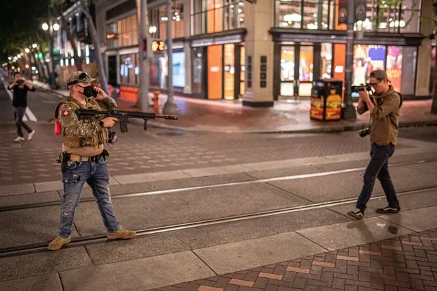 A far-right extremist points his rifle at Willamette Week journalist Justin Yau on August 8, 2021 in Portland, Oregon. After taking the man into custody, police later confirmed the rifle was a replica airsoft weapon. Anti-fascists and far-right extremists clashed near a religious gathering in downtown Portland for the second day in a row without a police response. (Photo by Nathan Howard/Getty Images)