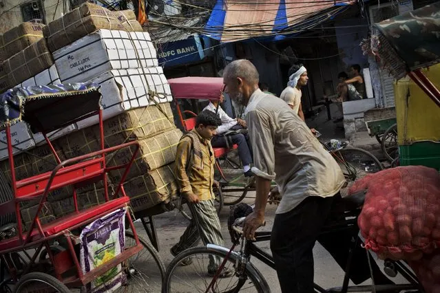 A man, center, pulls a wooden cart heavily loaded with goods as he maneuvers it through a market street crowded with cycle rickshaws and other commuters in New Delhi, India, Wednesday, July 22, 2015. (Photo by Bernat Armangue/AP Photo)
