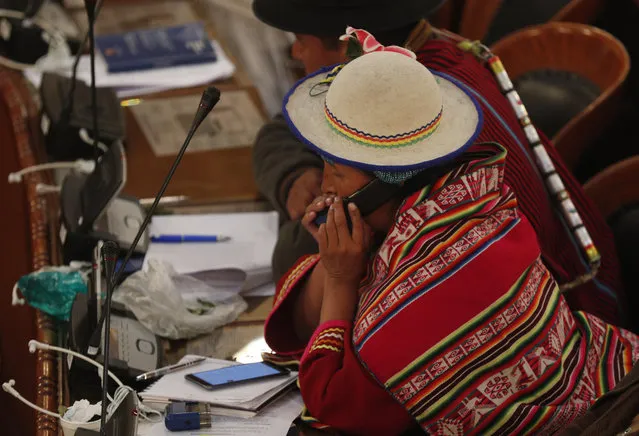 A lawmaker from the MAS party speaks on her cell phone in the Chamber of Deputies where lawmakers are debating a law that would give amnesty to former President Evo Morales in La Paz, Bolivia, late Thursday, December 5, 2019. The interim government of Bolivia warned that it will veto a legislative initiative that would grant an amnesty to Morales, currently exiled in Mexico, if approved by Congress where Morales' party MAS has majority. (Photo by Juan Karita/AP Photo)