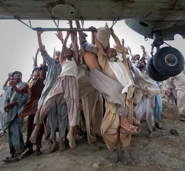 Marooned flood victims looking to escape, grab the side bars of a hovering Army helicopter which arrived to distribute food supplies in the Muzaffargarh district, Punjab province, Pakistan, August 7, 2010. (Photo by Adrees Latif/Reuters)