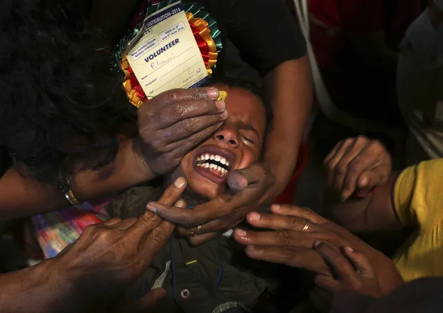 Volunteers try to open the mouth of a child suffering from asthma for a member of the Goud family to administer “fish medicine”, in Hyderabad, India, Wednesday, June 8, 2016. Started by the Bathini Goud family, the therapy is a secret formula of herbs, handed down by generations only to family members. The herbs are inserted in the mouth of a live sardine, or murrel fish, and slipped into the patient's throat. (Photo by Mahesh Kumar A./AP Photo)