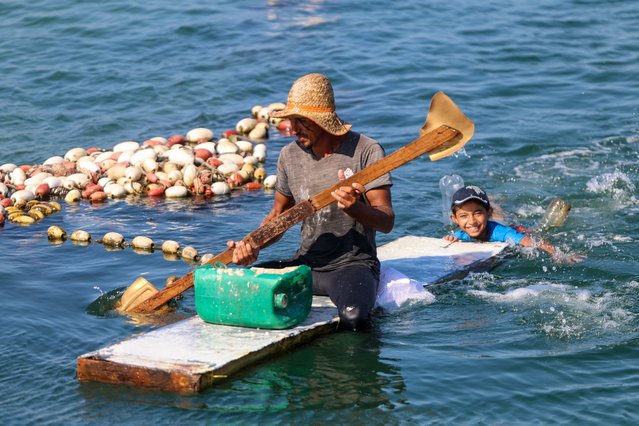 A fisherman paddles on a makeshift raft as a child swims behind him in Gaza City's main fishing harbour on September 7, 2024, amid the ongoing war between Israel and the Palestinian militant group Hamas. (Photo by Omar Al-Qattaa/AFP Photo)