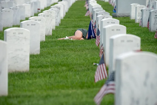 A woman lies in front of a grave in Section 60 at Arlington Cemetery in Arlington, Virginia, on May 29, 2022. (Photo by Stefani Reynolds/AFP Photo)