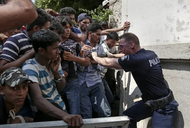 A Greek policeman tries to hold migrants behind a fence as they wait for a registration procedure outside a police station at southeastern island of Kos, Monday, August 10, 2015. Greece's coast guard rescued more than 1,400 migrants in nearly 60 search and rescue operations near several Greek islands in the eastern Aegean Sea over the past three days as the pace of new arrivals increase, authorities said MondayAugust 10, 2015. (Photo by Yorgos Karahalis/AP Photo)