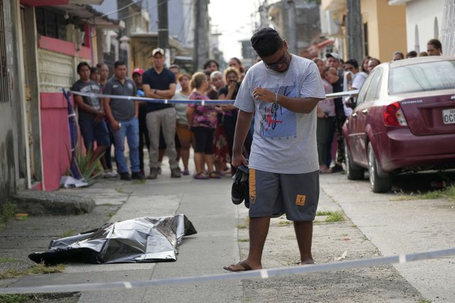 A person grieves near a covered body on the ground as residents watch from behind police tape in Duran, Ecuador, early Thursday, July 20, 2023. According to police, the body is that of a 20-year-old male who was shot to death. (Photo by Dolores Ochoa/AP Photo)