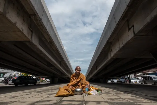 A Buddhist monk sits on the ground in between two vehicular overpasses as he waits to receive alms in northern Bangkok, Thailand on August 25, 2017. (Photo by Jerome Taylor/AFP Photo)