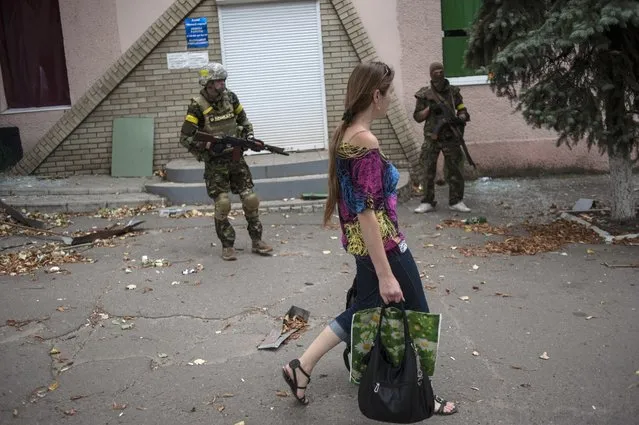 A woman walks past Ukrainian government soldiers from battalion “Donbass” guarding an entrance of a shop in village Mariinka near Donetsk, eastern Ukraine, Monday, August 11, 2014. The Red Cross will lead an international humanitarian aid operation into Ukraine’s conflict-stricken province of Luhansk with assistance from Russia, the European Union and the United States, Ukraine said Monday. (Photo by Evgeniy Maloletka/AP Photo)