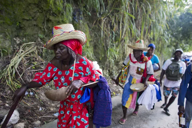 In this July 16, 2016 photo, Voodoo pilgrim Dieudone Beauvil, left, and her cousin Jesula Francois, following directly behind, walk from Mirebalais to Saut d' Eau, Haiti, to bathe in a waterfall believed to have purifying powers. After bathing in the waterfall they will throw away the garments they were wearing and put on new ones for good luck. (Photo by Dieu Nalio Chery/AP Photo)