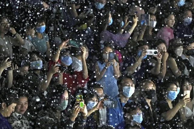 Fake snowflakes fall as spectators wearing face masks use their smartphones to film models present creations by Chinese designer Xiong Ying in her Heaven Gaia collection during the China Fashion Week in Beijing, Sunday, September 4, 2022. (Photo by Andy Wong/AP Photo)
