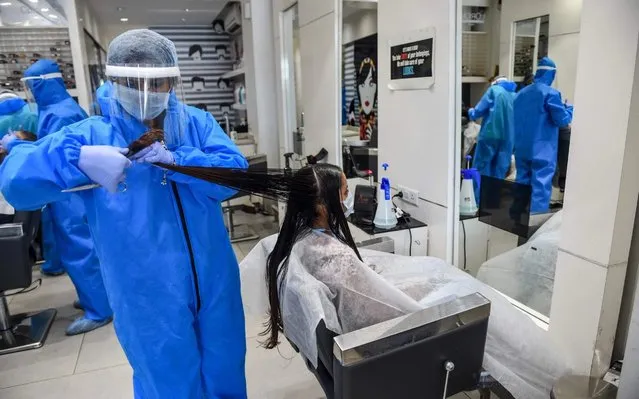 A worker wearing protective gear (L) as a precautionary measure against the COVID-19 coronavirus attends a customer at a hair and beauty salon located in an area declared as green zone for the pandemic, in Nadiad some 50 kms from Ahmedabad on May 17, 2020. (Photo by Sam Panthaky/AFP Photo)