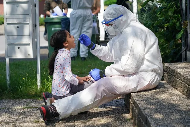 A worker with the German Red Cross (DRK) dressed in full PPE takes a throat swab sample from local resident Hadia, 8, in the village of St. Vit following a Covid-19 outbreak at the nearby Toennies meat packaging center during the coronavirus pandemic on June 23, 2020 near Guetersloh, Germany. State authorities announced today they are placing the entire Guetersloh region into lockdown following confirmed Covid-19 infection in over 1,500 employees of the plant. The Bundeswehr, the German armed forces, has stepped in to help test people at the approximately 250 houses and apartment complexes where Toennies employees, many of whom come from Romania, Bulgaria and Poland, live throughout the Guetersloh region. (Photo by Sean Gallup/Getty Images)