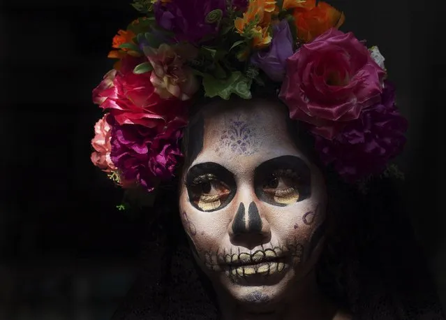A woman dressed as Mexico's iconic "Catrina" poses for tourists in Mexico City's main square, the Zocalo, as part of the Day of the Dead festivities in Mexico City, Friday, October 28, 2022. The holiday honors the dead as friends and family gather in cemeteries to decorate the graves of their loved ones. and hold a vigil during the night of November 1 and 2. (Photo by Marco Ugarte/AP Photo)
