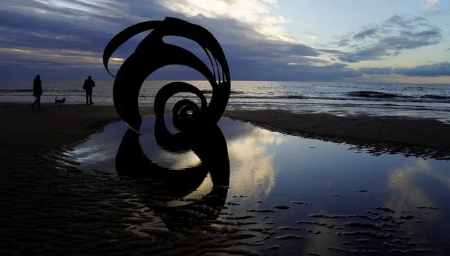 People walk past a metal sculpture of a shell at sunset on Cleveleys Beach, Britain, October 26, 2017. (Photo by Phil Noble/Reuters)