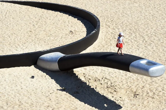 A girl walks on the handle of a 24 meter giant frying pan by Australian artist Andrew Hankin, an artwork titled “We're fryin' out here” at Tamarama beach, part of a selection of artworks featured in the annual Sculpture by the Sea on the ocean walk between Bondi Beach and Tamarama Beach in Sydney, Australia, 23 October 2014. (Photo by Dean Lewins/EPA)