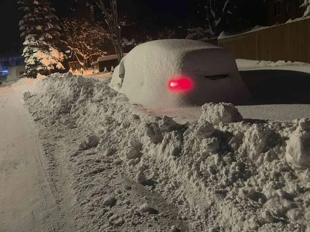 A car buried under snow and plowed in warms up Friday, December 9, 2022, in Anchorage, Alaska. A winter storm dumped up to 2 feet of snow in the city of Anchorage this week, closing schools for three days in the state's largest city and causing headaches for some drivers. (Photo by Mark Thiessen/AP Photo)
