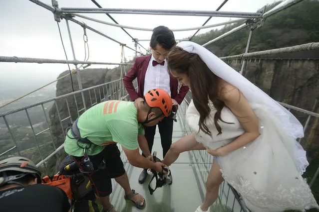 A pair of newlyweds wear protective equipment during their wedding on a glass-bottomed suspension bridge 180 meters over a vally at Shiniuzhai National Geopark in Pingjiang County on August 9, 2016 in Yueyang, Hunan Province of China. (Photo by VCG/VCG via Getty Images)