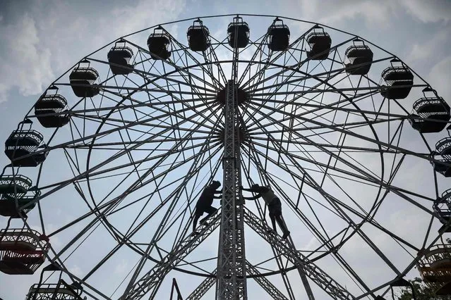Workers are silhouetted as they work on a giant Ferris wheel as it is being set up at a ground ahead of an exposition in Chennai on December 20, 2022. (Photo by Arun Sankar/AFP Photo)