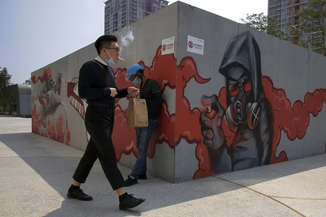 A man lowers his mask to smoke as he walks past graffiti artwork in Beijing Monday, July 13, 2020. China reported eight new cases, all of them brought from outside the country, as domestic community infections fall to near zero. (Photo by Ng Han Guan/AP Photo)