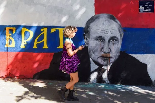 A woman walks next to a mural of Russian President Vladimir Putin with the word 'Brother' written on it, which has been vandalised with red spray paint, following Russia's invasion of Ukraine, in Belgrade, Serbia on June 20, 2022. (Photo by Zorana Jevtic/Reuters)