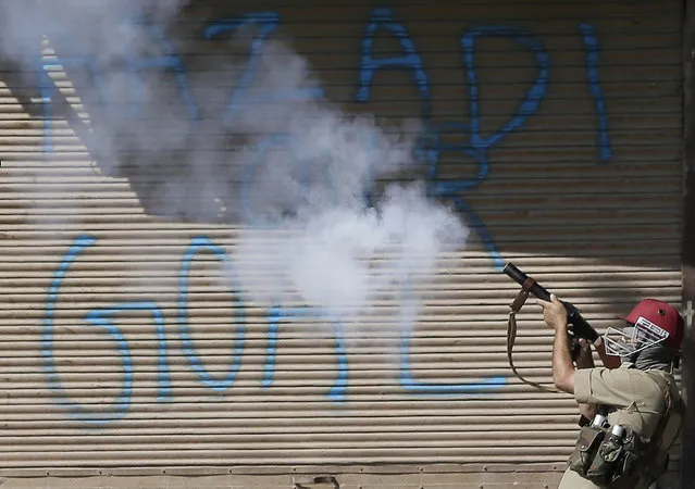 An Indian policeman fires a tear gas shell on Kashmiri protesters in front of a grafiti on shutters that reads “Freedom our goal”, in Srinagar, Indian controlled Kashmir, Friday, September 23, 2016. Kashmir is witnessing the largest protests against Indian rule in recent years, sparked by the July 8 killing of a popular rebel commander by Indian soldiers. (Photo by Mukhtar Khan/AP Photo)