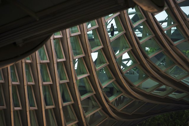 A woman walks across the window panels of the Phoenix Center, in Beijing, Wednesday, July 23, 2025. (Photo by Andy Wong/AP Photo)