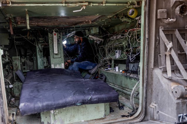 Yahya Akhzeiq, 27-years-old, connects a mobile phone to a charger as he sits in a converted Israeli military vehicle abandoned by the Israeli army and now used by the mainly displaced Palestinian communities as a charging point for mobiles and laptops, in Tel al-Hawa neighborhood, in the southern part of Gaza City on November 29, 2025. Brothers Yahya and Akram Akhzeiq, have set-up a charging point using solar-energy panels placed on the exterior the vehicle's hull, which  sits under the concreate of a destroyed building. The majority of Gaza's 2.4 million people have been displaced, often multiple times, by the war that began with Hamas's attack on southern Israel on October 7, 2023. With many displaced living in tent camps, the coming winter is raising serious concerns. (Photo by Omar Al-Qattaa/AFP Photo)