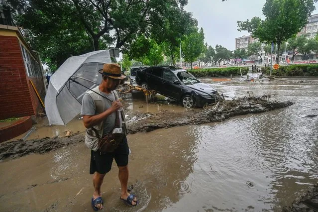 A man stands near a damaged car after heavy rains in Mentougou district in Beijing on August 1, 2023. (Photo by Pedro Pardo/AFP Photo)