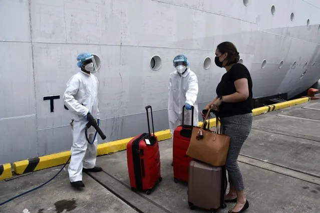 A healthcare worker disinfects the luggage of an evacuee before boarding the Royal Caribbean cruise ship Reflection, in Kingstown, on the eastern Caribbean island of St. Vincent, Friday, April 16, 2021. La Soufriere volcano has shot out another explosive burst of gas and ash Friday morning as the cruise ship arrived to evacuate some of the foreigners who had been stuck on a St. Vincent island by a week of violent eruptions. (Photo by Orvil Samuel/AP Photo)