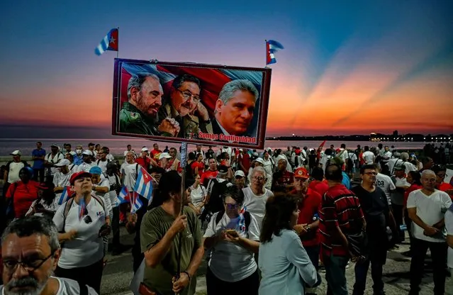 A demonstrator carries a poster with images of late Cuban president Fidel Castro, Cuban former president Raul Castro, and Cuban president Miguel Daz Canel during the commemoration of May Day (Labour Day) to mark the international day of the workers in Havana on May 5, 2023. Without the mass mobilization of yesteryear, this Friday's Workers' Day rally was held in Havana in a reduced version and four days late, overshadowed by the serious fuel crisis facing the island. (Photo by Yamil Lage/AFP Photo)