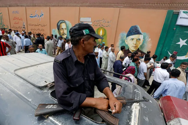 A police officer guards, where electoral workers stand in line to collect election materials ahead of general election in Karachi, Pakistan July 24, 2018. (Photo by Akhtar Soomro/Reuters)