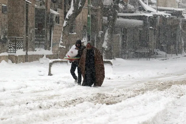Syrians walk in a snow covered street in the town of Maaret al-Numan, in Syria's northern province of Idlib, on December 21, 2016. Rebels and civilians who have sought refuge in the opposition-held province of Idlib, most recently from second city Aleppo, say they are suffering from skyrocketing prices and overpopulation. At least 25,000 people, including rebel fighters, have left east Aleppo since last week under an evacuation deal that will see the city come under full government control. (Photo by Mohamed al-Bakour/AFP Photo)