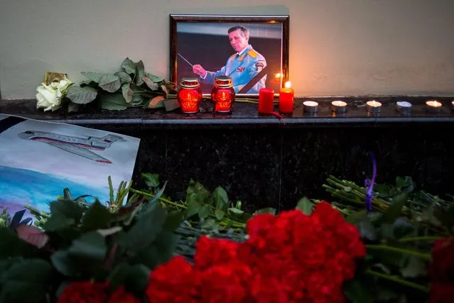 A picture shows a portrait of Valery Khalilov, Chief conductor and artistic director of Alexandrov song and dance ensemble placed next to candles, flowers and a drawing of a plane at the home stage building of the Alexandrov Ensemble (The Red Army Choir), in Moscow, on December 25, 2016, after a Russian military plane which included dozens of Red Army Choir members crashed. The Russian military plane crashed on its way to Syria on December 25, with no sign of survivors among the 92 onboard, who included dozens of Red Army Choir members heading to celebrate the New Year with troops. Russia's defence ministry said a body had been recovered from the Black Sea. (Photo by Alexander Utkin/AFP Photo)
