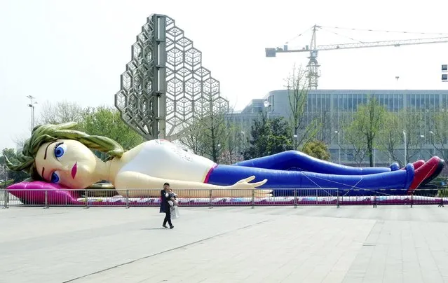 A woman holding her child walks past a giant inflated doll in the shape of a woman, on a square in Nanjing, Jiangsu province April 9, 2015. (Photo by Reuters/Stringer)
