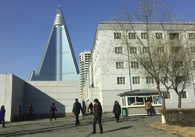 In this December 11, 2016 photo, residents pass by the towering Ryugyong Hotel in Pyongyang, North Korea. Thirty years after work began on what was then one of the tallest hotel projects ever attempted, the inside of the structure has yet to be completed and mystery swirls over whether it ever will ever open for guests. (Photo by Eric Talmadge/AP Photo)
