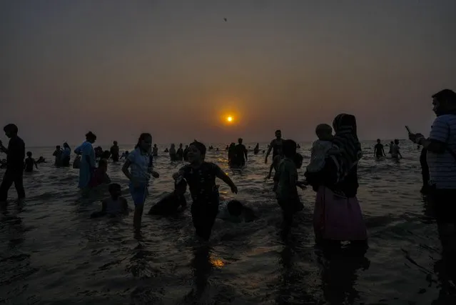 People gather at the Juhu Beach on the Arabian Sea coast as the sun sets on New Year's eve in Mumbai, India, Sunday, December 31, 2023. (Photo by Rafiq Maqbool/AP Photo)