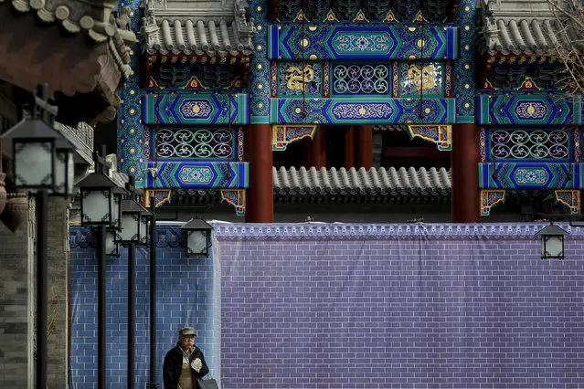 In this February 25, 2019, photo, a man eats bread as he walks by a wall covering a deserted commercial building structure along a hutong alley near Qianmen Avenue, a popular tourist spot in Beijing. (Photo by Andy Wong/AP Photo)