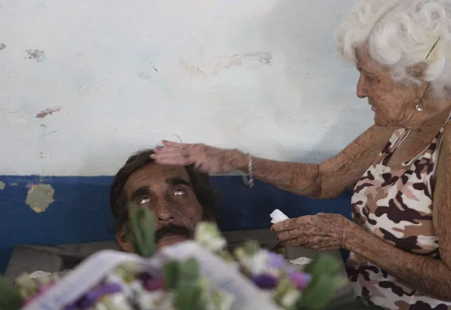In this February 5, 2014 photo, Divaldo Aguiar, who plays the part of Pachencho, in a mock funeral known as the Burial of Pachencho, lies inside a coffin as Carmen Zamora, who plays the part of his widow, puts her hand on his head, at a cemetery in Santiago de Las Vegas, Cuba. (Photo by Franklin Reyes/AP Photo)