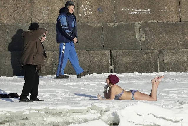 A man takes a photo of a woman sunbathes on snow near the wall of St.Peter and Paul Fortress in St.Petersburg, Russia, Tuesday, February 7, 2017. The temperature in St. Petersburg is minus 12 degrees Centigrade (10 degrees Fahrenheit). (Photo by Dmitri Lovetsky/AP Photo)