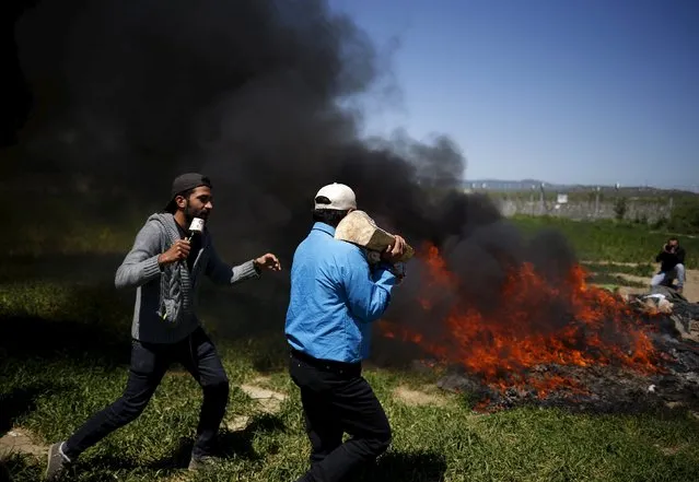 Men jokingly present themselves as TV crew in front of burning blankets in a field near a makeshift camp for migrants and refugees at the Greek-Macedonian border near the village of Idomeni, Greece, April 21, 2016. (Photo by Stoyan Nenov/Reuters)