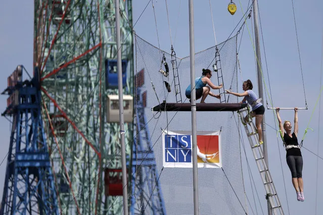 A student of the Trapeze School New York in Coney Island, right, flies with the Wonder Wheel in the background, Friday, July 3, 2015, in the Brooklyn borough of New York. The school will be open 7 days a week until it is too cold to fly. Temperatures will be in the mid 70s and 80s for the 4th of July holiday weekend. (Photo by Mary Altaffer/AP Photo)