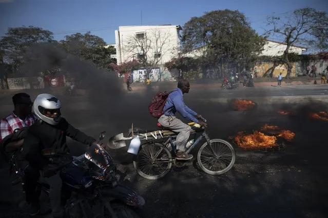 A bicyclist pedals past burning tires set on fire by factory workers demanding a salary increase, in Port-au-Prince, Haiti, Thursday, February 10, 2022. The workers employed at factories that produce textiles and other goods say they make 500 gourdes ($5) a day for nine hours of work and are seeking a minimum of 1,500 gourdes ($15) a day. (Photo by Joseph Odelyn/AP Photo)