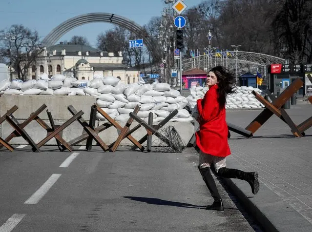 A woman runs across the street next to an anti-tank constructions in central Kyiv, Ukraine on March 10, 2022. (Photo by Gleb Garanich/Reuters)