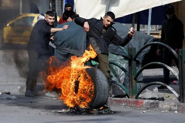 A Palestinian demonstrator kicks a burning tyre during a protest over the killing of three Palestinian gunmen by Israeli forces, in Hebron in the Israeli-occupied West Bank on February 9, 2022. (Photo by Mussa Qawasma/Reuters)