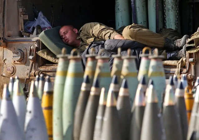 An Israeli soldier sleeps on a truck behind mobile artillery unit shells at a position on the Israel-Gaza border, July 11, 2014. Gaza rocket fire struck a gas station and set it ablaze in southern Israel, seriously wounding one person in the four-day-long offensive. (Photo by Lefteris Pitarakis/AP Photo)