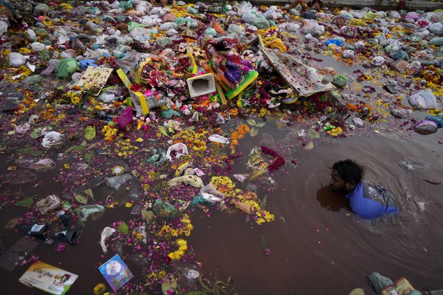 A man searches for reusable material amid idols of Hindu goddess Dashama immersed by devotees in River Sabarmati in Ahmedabad, India, Thursday, July 27, 2023. Every year Hindu devotees in this western state of Gujarat immerse idols of goddess Dashama after worship marking the end of the ten-days long Dashama festival. (Photo by Ajit Solanki/AP Photo)